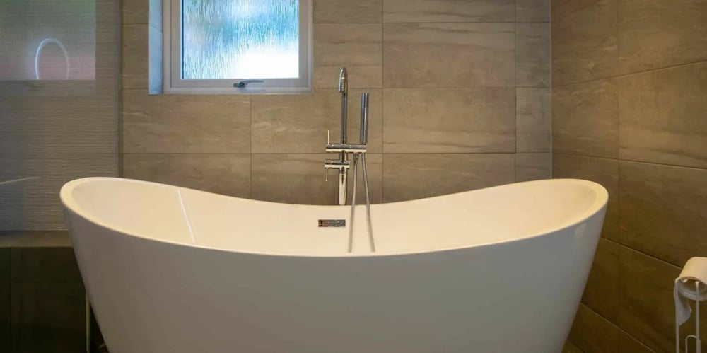 Freestanding bath with chrome fittings and warm neutral tiles in a bathroom completed by Claude’s Tradesmen