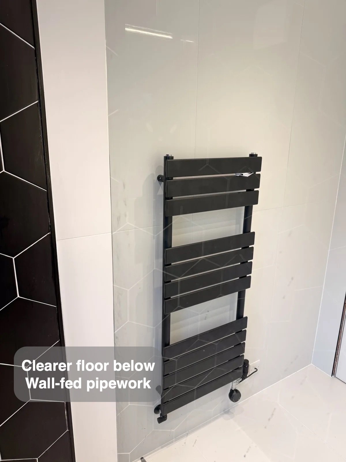 Black towel radiator on pale tiled wall