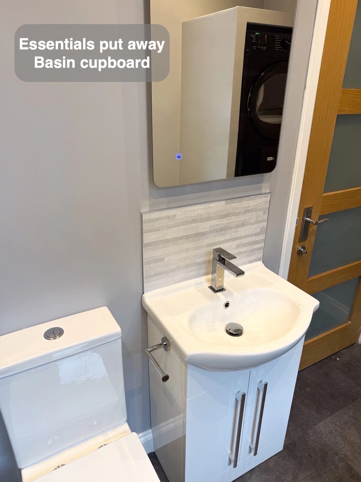 Basin cupboard and illuminated mirror beside toilet